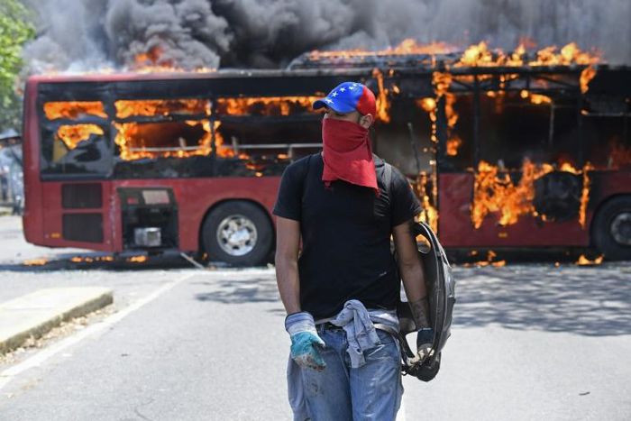 An opposition demonstrator walks by a flaming bus during clashes with soldiers loyal to Venezuelan President Nicolas Maduro in Caracas