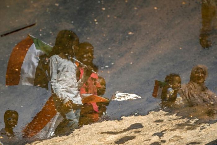 A reflection in a puddle of Sudanese protesters as they carry national flags outside the army headquarters in the capital Khartoum on Saturday
