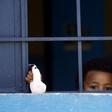 A child from a family of African migrants peeks out from a window at Libyan detention center, among thousands who have tried in recent years to flee to Europe via the North African country
