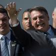 Brazilian President Jair Bolsonaro (R) waves next to his son Flavio, a federal senator who denies any impropriety after a report that he allegedly made more than three million reais ($790,000) buying and selling 19 apartments and commercial locations i...