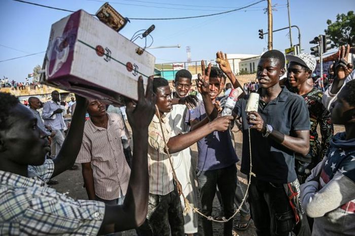 Young Sudanese protesters mimic journalists -- complete with a cardboard mocked up camera and a plastic bottle to represent a microphone -- to poke fun at state TV for failing to cover demonstrations