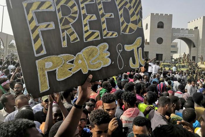 Sudanese anti-regime demonstrators holding up a banner calling for "Freedom, Peace and Justice" around the army headquarters in Khartoum