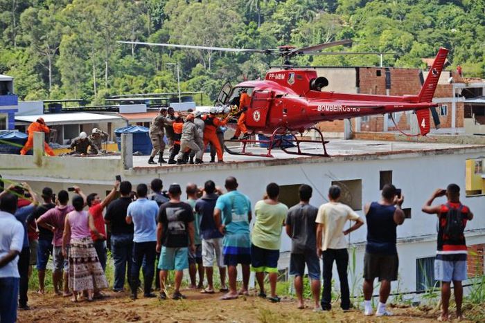 People watch as an injured person is carried onto a rescue helicopter after two buildings collapsed in Muzema, Rio de Janeiro, Brazil