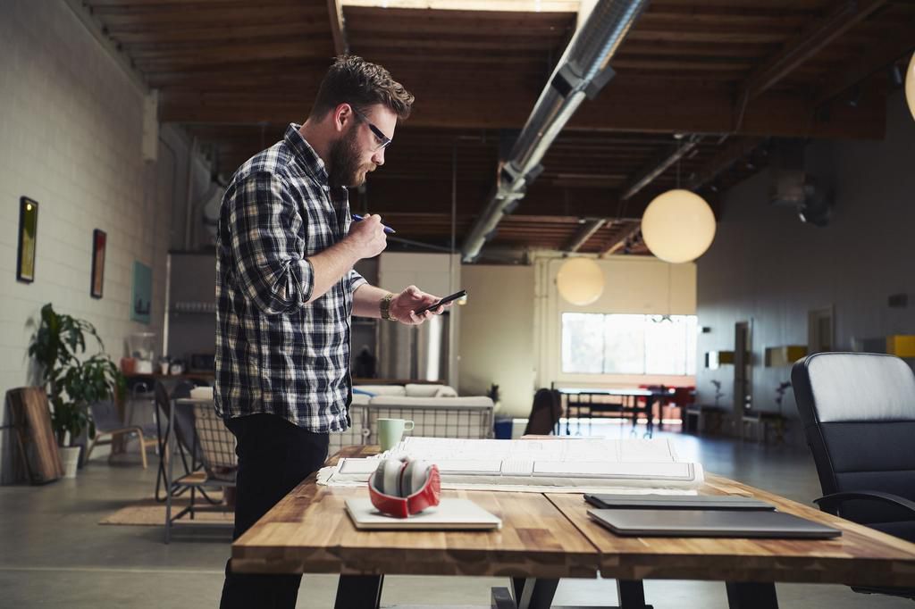 Architect standing at desk looking at mobile phone