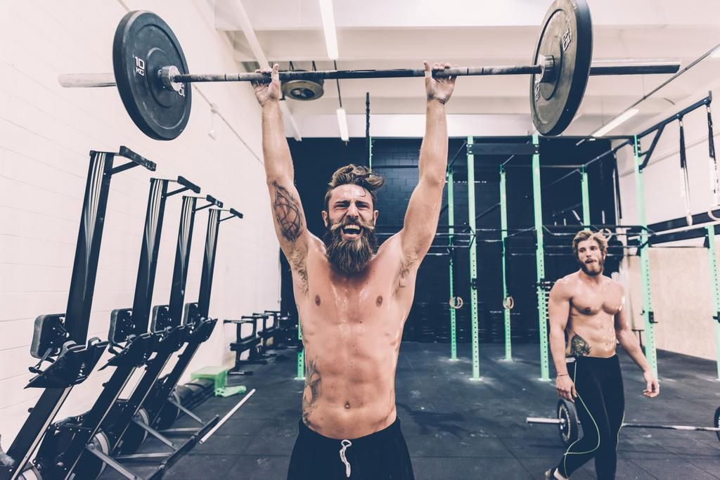Young male cross trainer snatch lifting barbell in gym