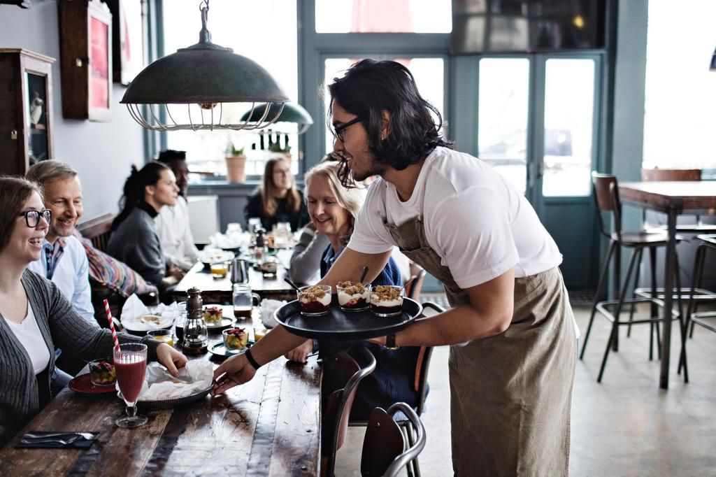 Waiter serving food to smiling customers at restaurant