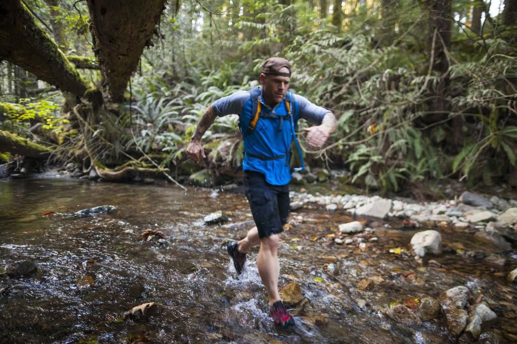 Man trail running across stream in forest near Elbow Lake in Fraser Valley, Harrison Mills, British Columbia, Canada