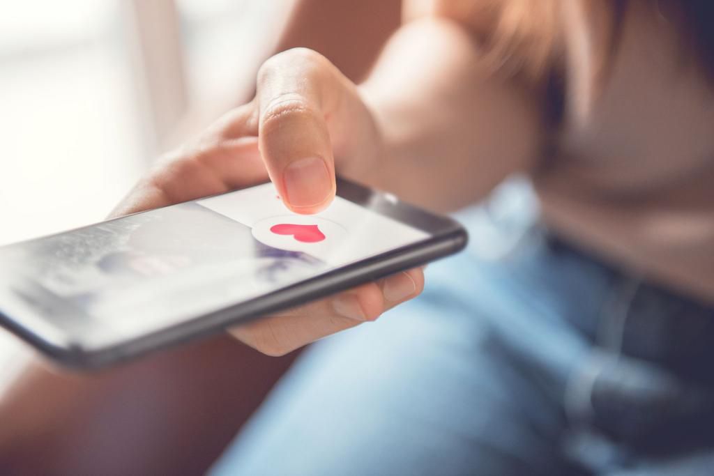 Finger of woman pushing heart icon on screen in mobile smartphone application. Online dating app, valentine's day concept.