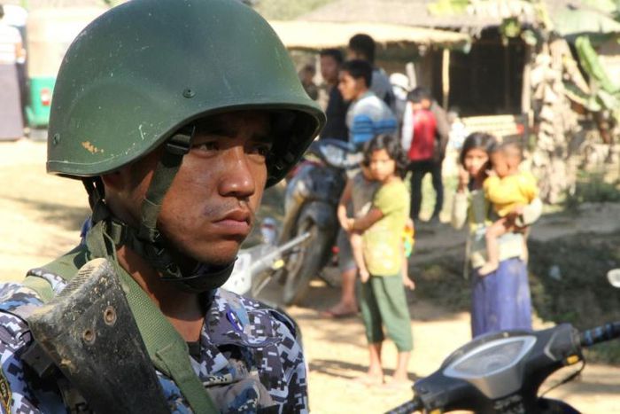 A Myanmar border guard stands near a group of Rohingya Muslims in front of their homes in restive Rakhine state. The military has poured thousands of troops into the area to put down an insurgency