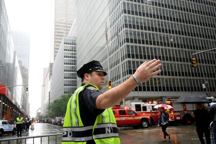 A policeman gestures near fire trucks after a helicopter crash-landed on top of a building in midtown Manhattan on June 10, 2019