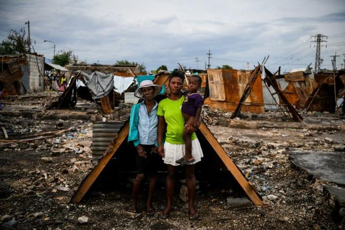 Iris Daniel, 57, Lovely Saint-Pierre, 32, and Evanston Daniel, 5, pose on May 25, 2019, outside a makeshift shelter on the site of their home which was burned during a November 2018 gang war in Port-au-Prince