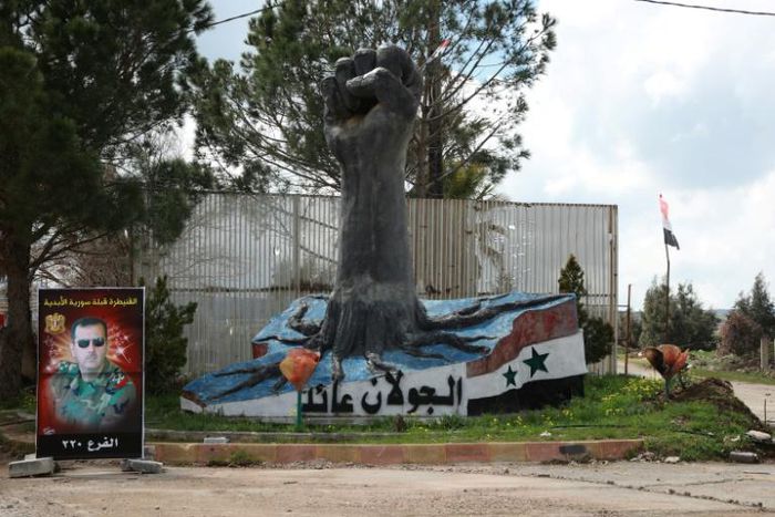 A portrait of Syrian President Bashar al-Assad stands near a sculpture in the Syrian town of Quneitra, in the Golan Heights
