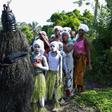 Young girls in white face paint take part in a procession to start their initiation into the Bondo secret society, alongside a figure called the Black Devil