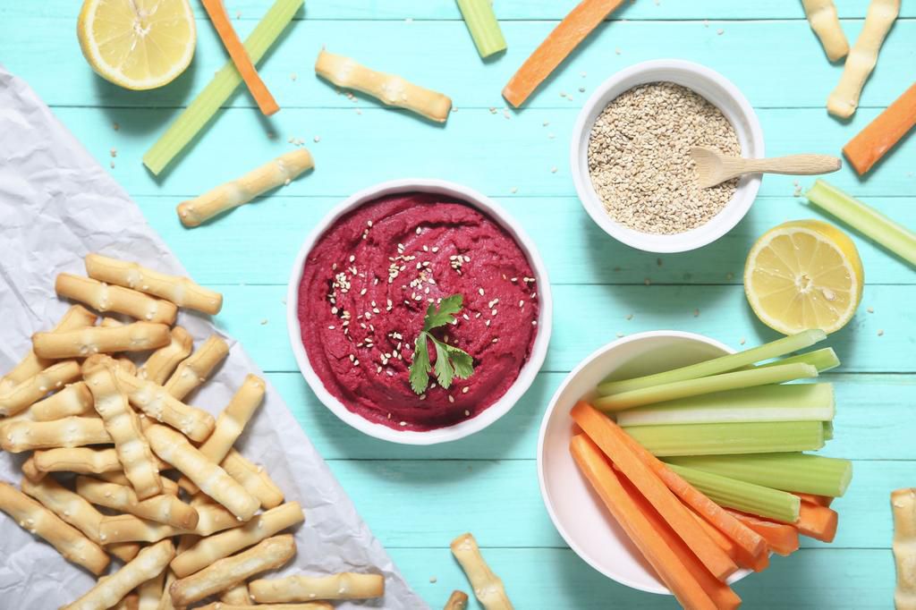 Bowl of beetroot hummus, sesame, carrot and celery crudites and breadsticks