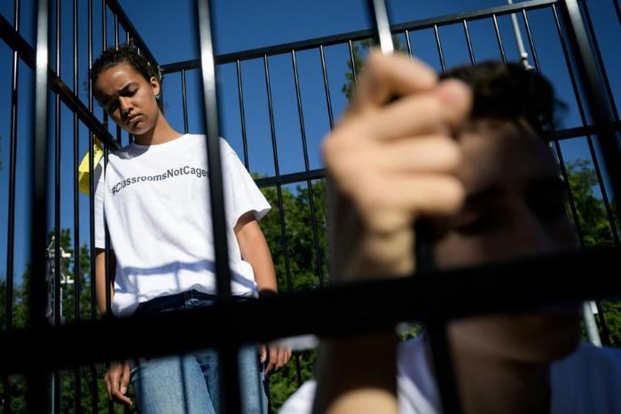 Three teens wearing t-shirts with "#ClassroomsNotCages" scrawled across the front stood inside a small cage erected outside the gates of the United Nations's European headquarters