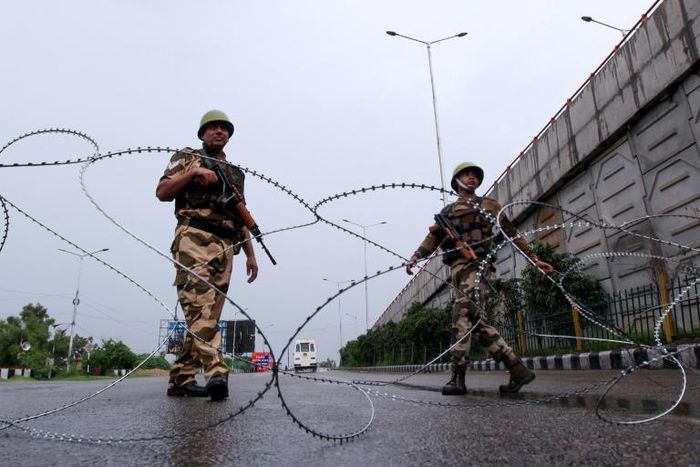 Security personnel stand guard at a roadblock on a near-deserted street in Jammu, Kashmir