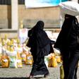 A Yemeni woman carries a sack of grain on her head while walking after receiving food aid provided by a local charity
