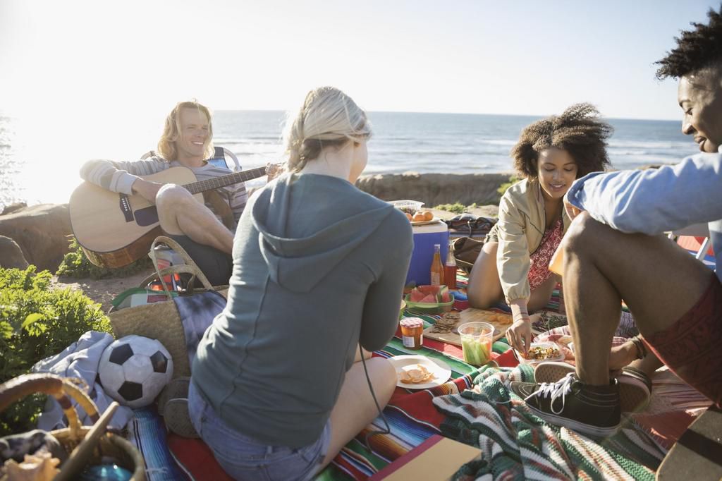 Young friends hanging out, enjoying picnic on sunny beach