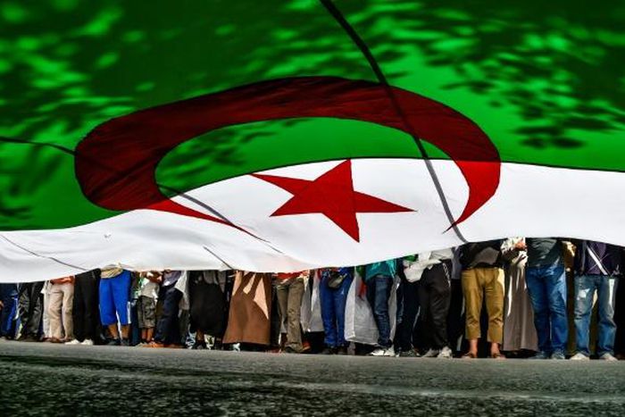 In this file photo from late May, Algerian protesters are seen from underneath a giant national flag