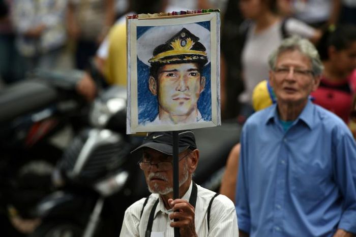 A man in Caracas holds up a portrait of Venezuelan retired naval officer Rafael Acosta, who was allegedly tortured before his death