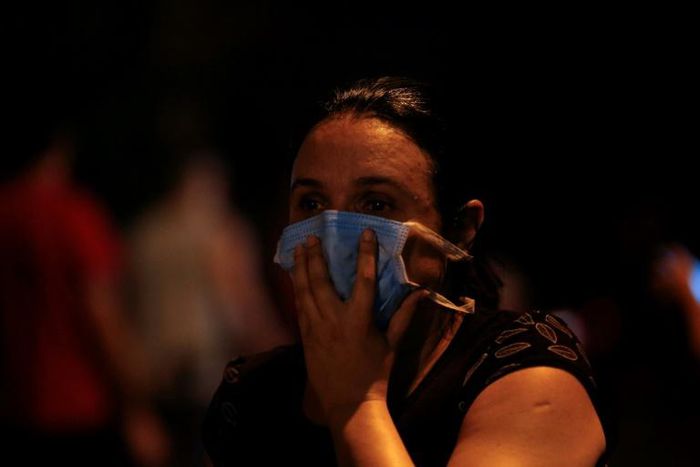 A woman covers her face with a surgical mask to protect herself from the smoke during a fire at the Badim hospital in Rio de Janeiro