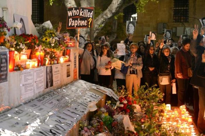People hold portraits as they stand beside lighted candles placed in memory of murdered journalist Daphne Caruana Galizia on the sixth month anniversary of her death at a makeshift memorial outside the law courts in Valletta, Malta on April 16, 2018