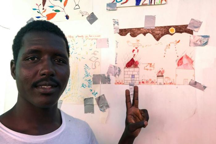 A rescued migrant Arun Mohamed next to his drawing of war in Sudan's Darfur region