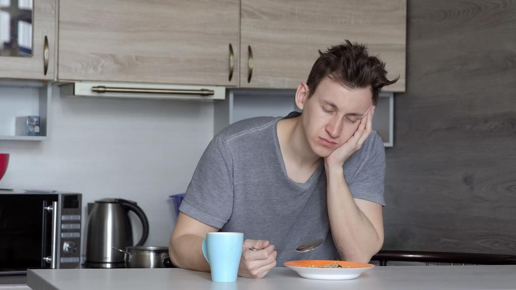 Beautiful sleepy man having breakfast at the table