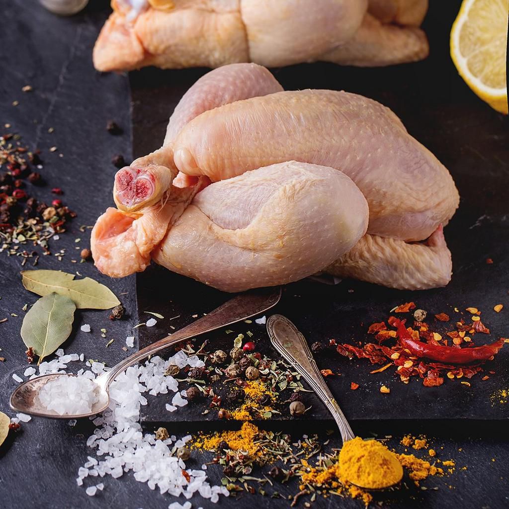Two Raw mini Chicken with sea salt and different spices over black slate board