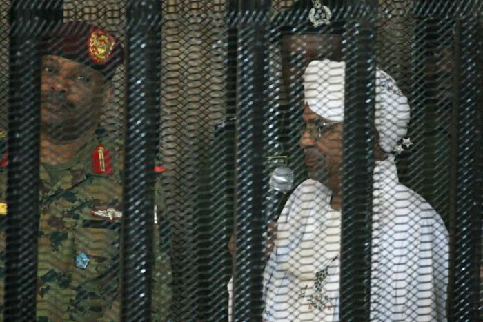 Sudan's deposed military ruler Omar al-Bashir stands in a defendant's cage at the opening of his corruption trial in Khartoum in August