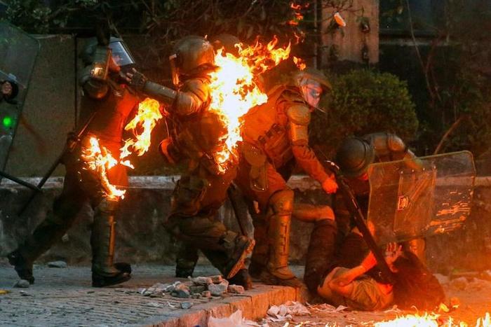 A demonstrator is held while a petrol bomb hits riot police during a protest against the government in Santiago on Friday