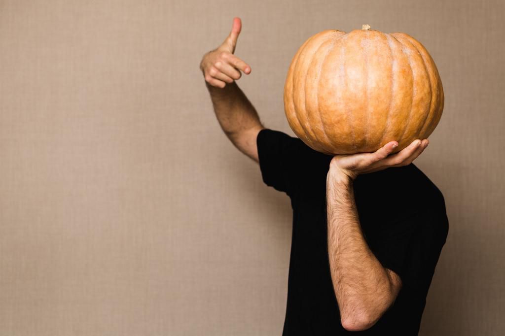 Young man in black t-shirt holding big pumpkin in front of his face