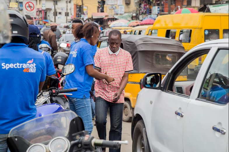 A female canvasser providing flyer to a passer-by on Obafemi Awolowo Way, Ikeja during the road show organised to leverage the new Spectranet Experience Centres.