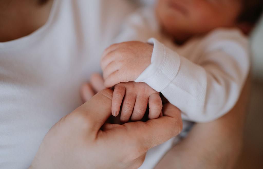 A midsection of a mother holding a newborn baby son at home. A close-up.