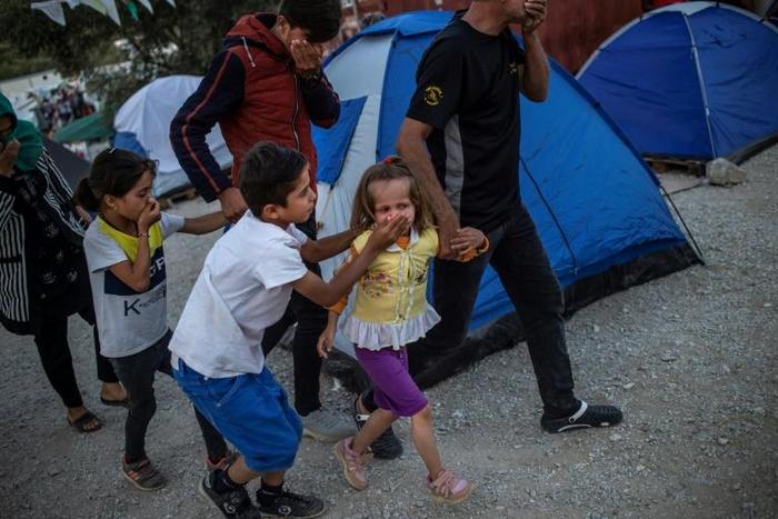 Migrants shield their mouths from tear gas during clashes at the Moira refugee camp