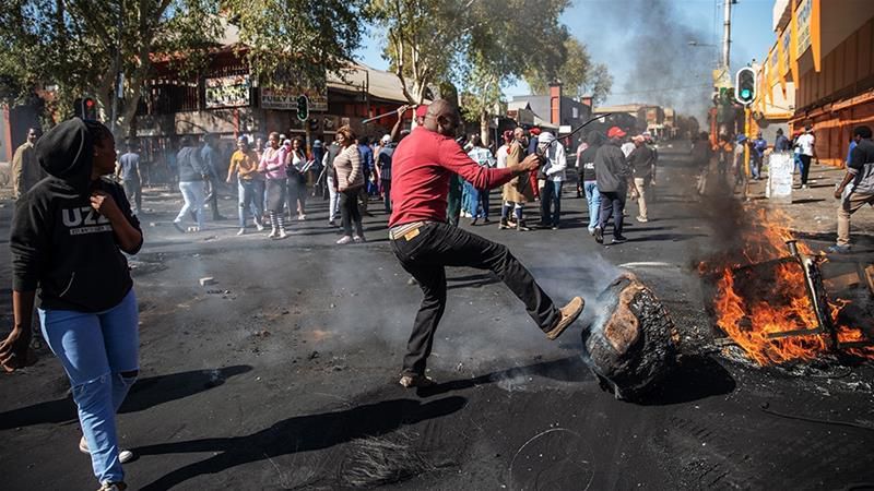 A man kicks a burning piece of furniture during a riot in the Johannesburg suburb of Turffontein on September 2, 2019 [Michele Spatari/AFP]
