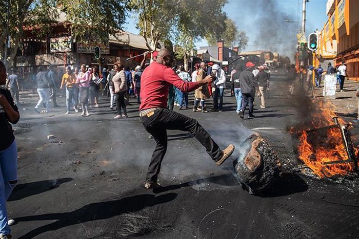 A man kicks a burning piece of furniture during a riot in the Johannesburg suburb of Turffontein on September 2, 2019 [Michele Spatari/AFP]