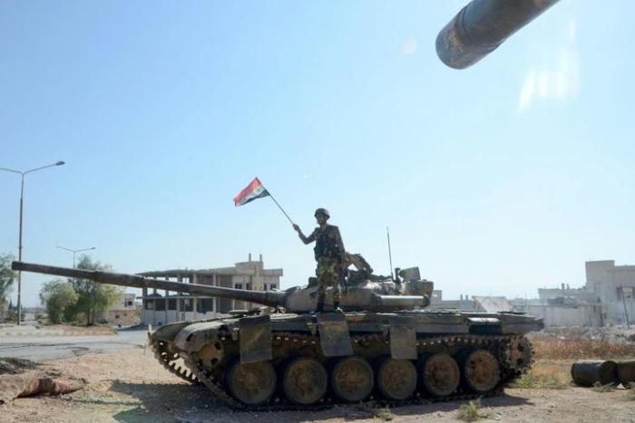 A Syrian soldier waves a national flag atop a tank in the strategic town of Khan Sheikhun on Saturday