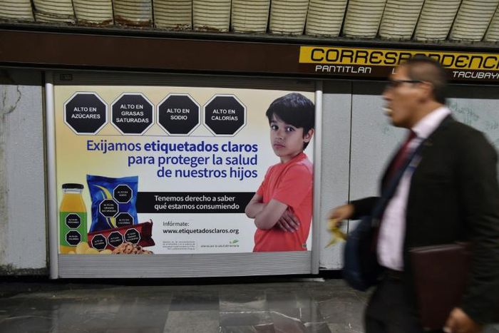 "We demand clear labeling to protect the health of our children," reads the sign in the Mexico City subway, which shows sample junk food warnings of black hexagons with white lettering