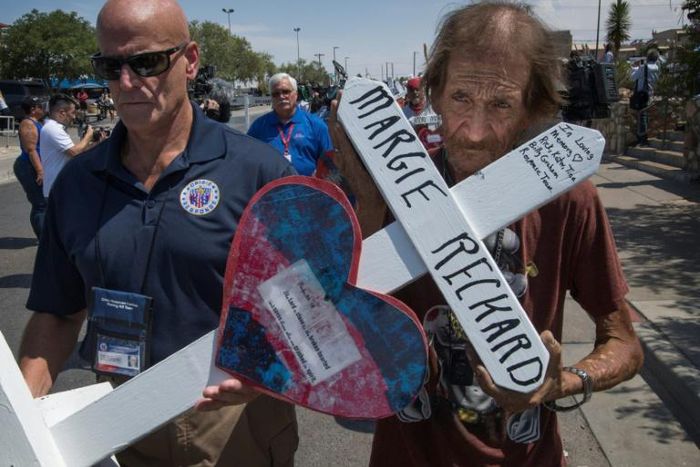 Antonio Basco (R) holds the cross of his common-law wife Margie Reckard who died in the El Paso shooting, as he walks to a makeshift memorial after the shooting that left 22 people dead