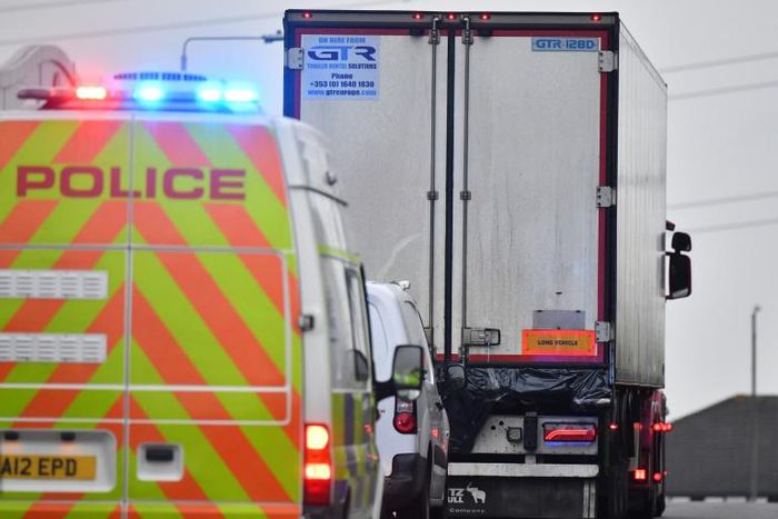 Police drive away a lorry, with black plastic visible at the rear, in which 39 dead bodies were discovered, sparking a murder investigation