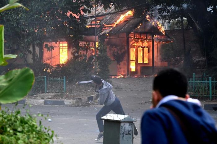 A building goes up in flames in Jakarta as a protester hurls rocks at police during violent demonstrations against the government's proposed change to the criminal code