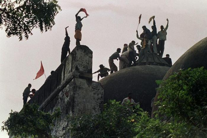 Hindu fundamentalists shout and wave banners as they stand on the top of a stone wall and celebrate the destruction of the 16th century Babri Mosque in Ayodhya in 1992
