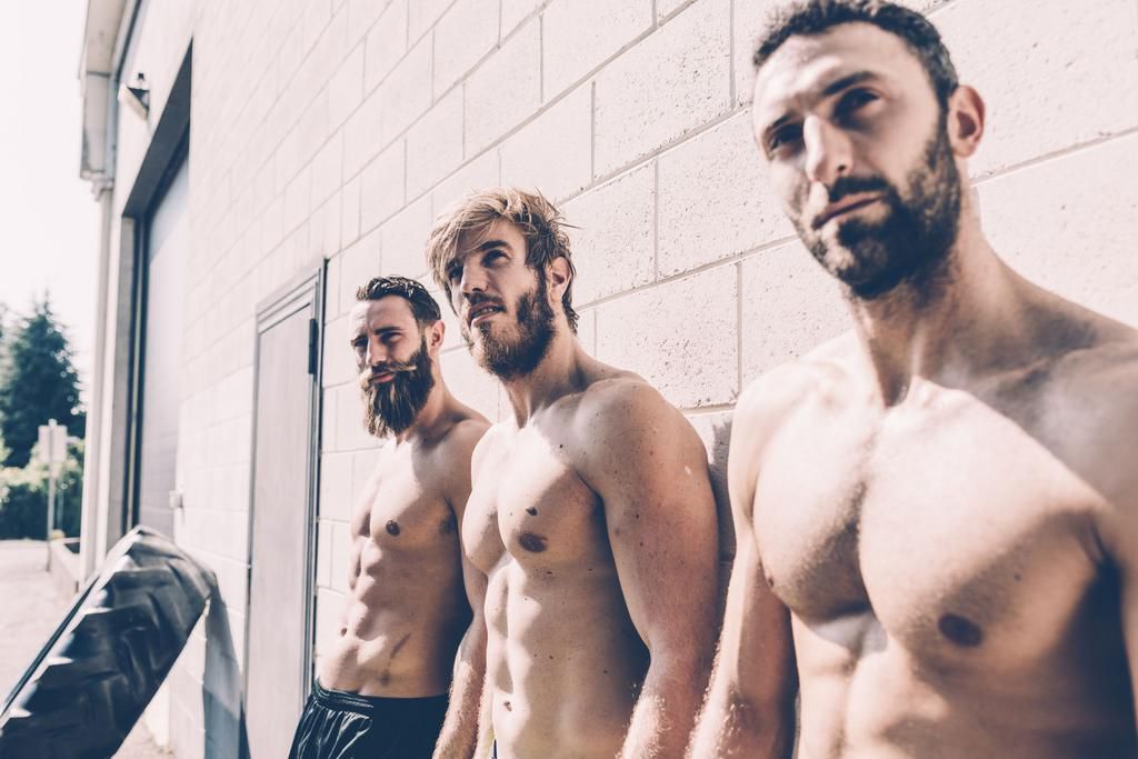 Three bare-chested male cross trainers leaning against wall outside gym