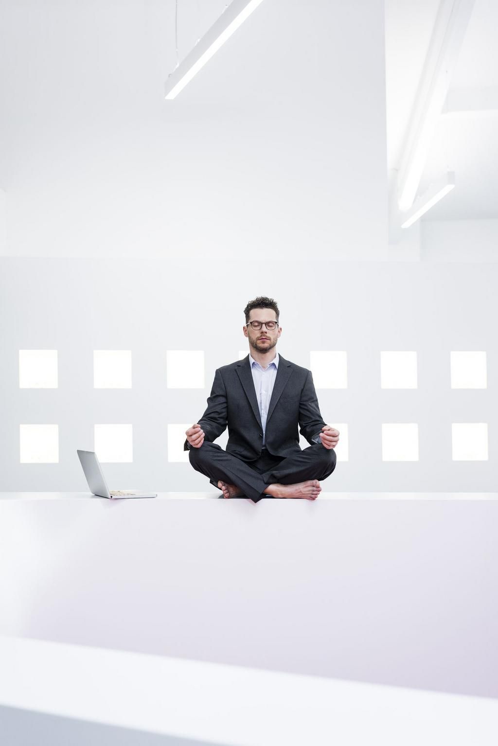 Businessman doing yoga in office next to laptop