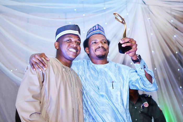 Senator Elisha Abbo (right) raises his "Beacon of Hope" award. "Beacon of Hope" was his campaign slogan before he was elected as the youngest senator in the 9th Senate. Weeks before his inauguration, he beat up and arrested a woman for telling him to c...