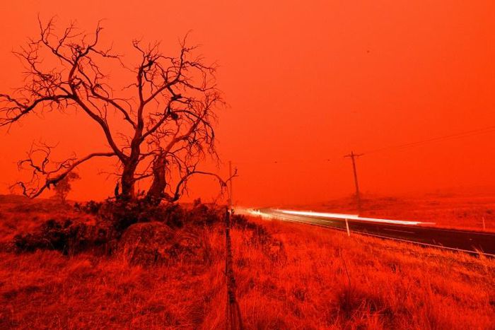 A long exposure picture shows a car commuting on a road as the sky turns red from smoke of the Snowy Valley bushfire on the outskirts of Cooma