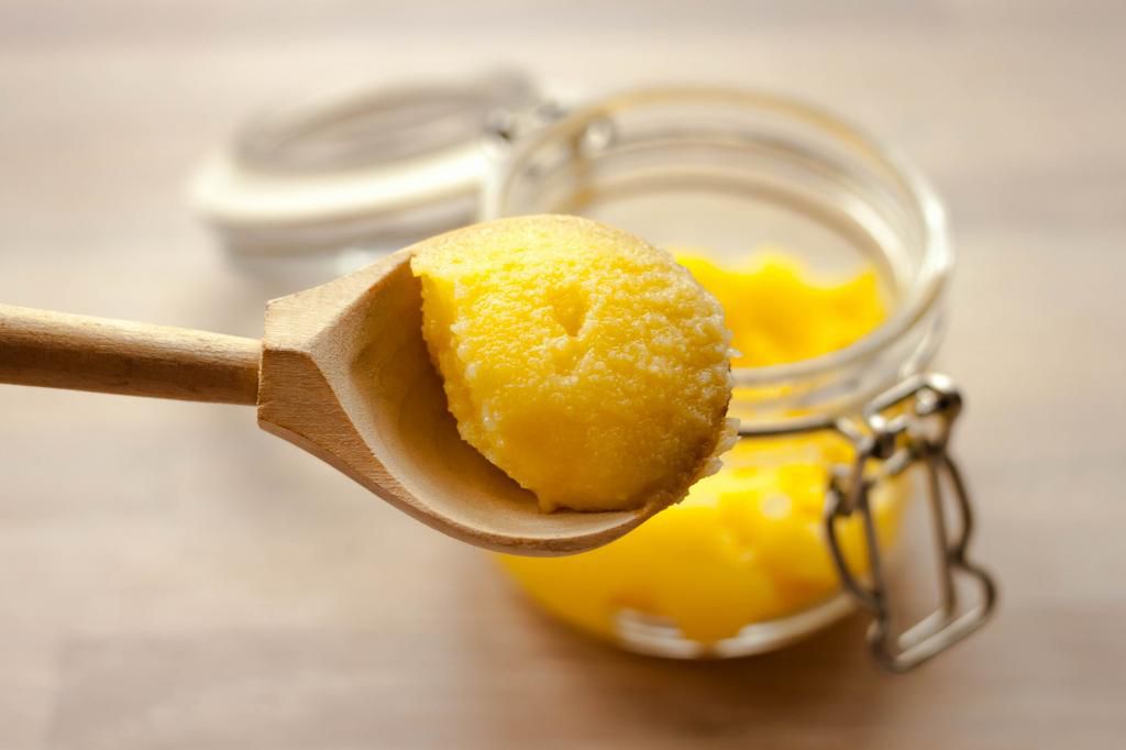 Ghee clarified butter desi in glass jar with spoon made from wood on natural wooden background