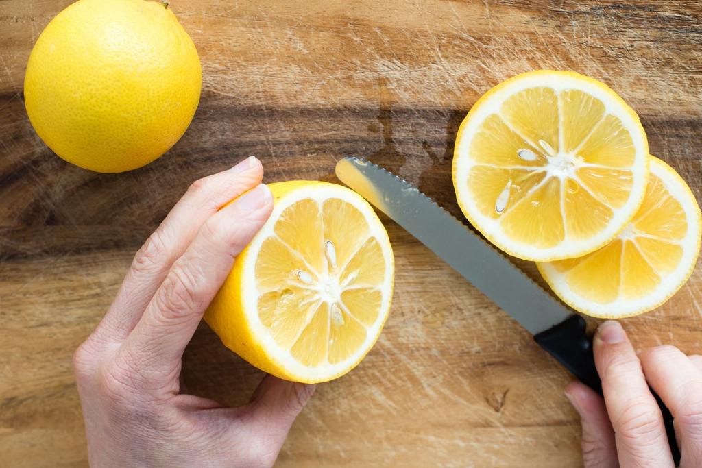 Cropped Image Of Hand Cutting Lemon On Cutting Board