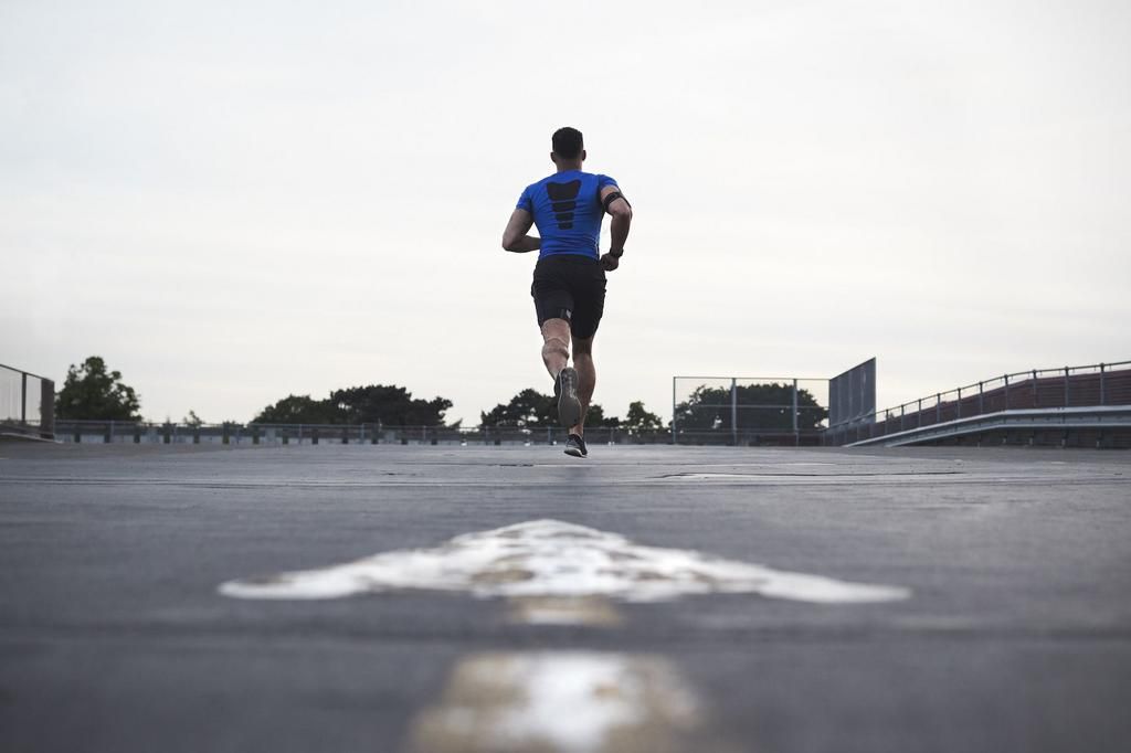 Male athlete running on a road away from camera, full length